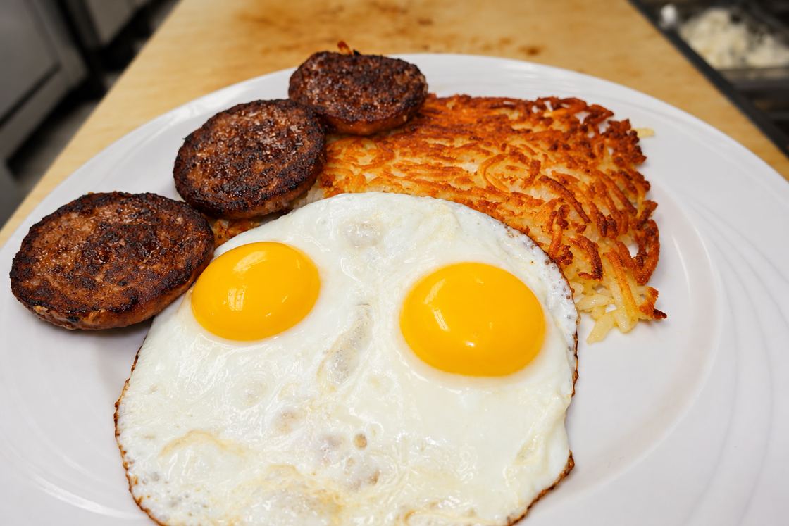 Two sunny-side-up eggs with sausage patties and crispy homemade hash browns