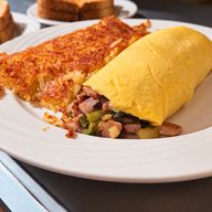 Golden three-egg omelette filled with ham, green pepper and onion, next to crispy homemade hash browns, with toast behind